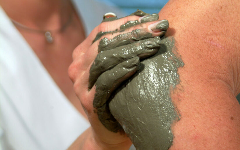 Therapeutin verteilt Heiulschlamm auf dem Ellebogen eines Patienten