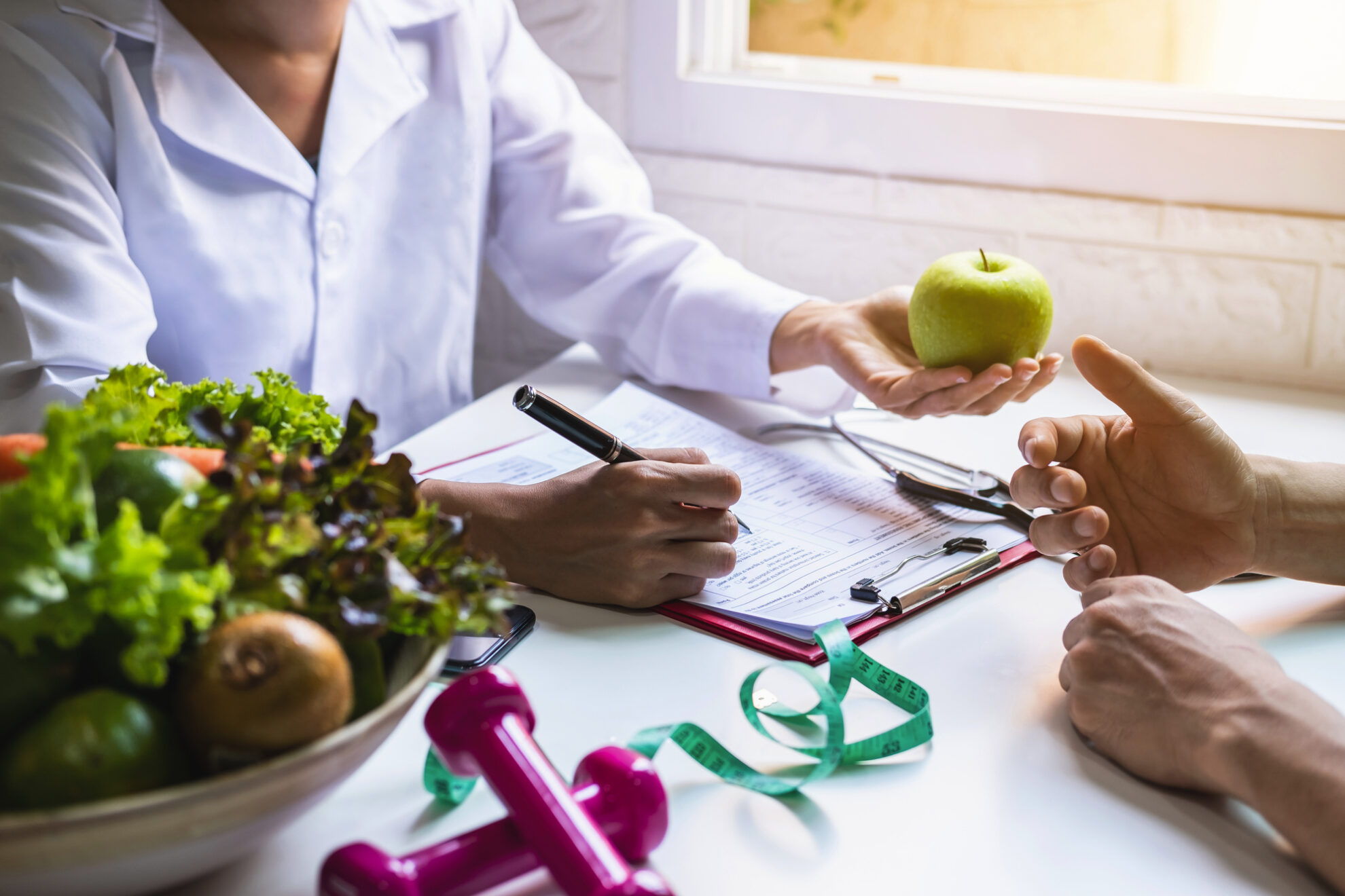 Ernährungsberatung_Kurdirekt Ernährungsberaterin im weißen Kittel beim Gespräch mit einem Patienten reicht ihm einen Apfel
