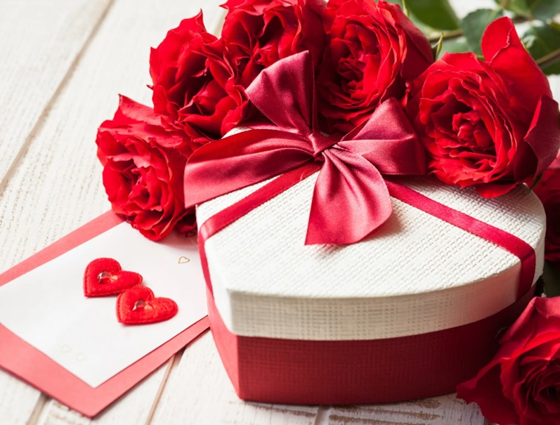 Bild zeigt rote Rosen, eine Dose in Form eines Herzens und eine Karte für Valentinstag